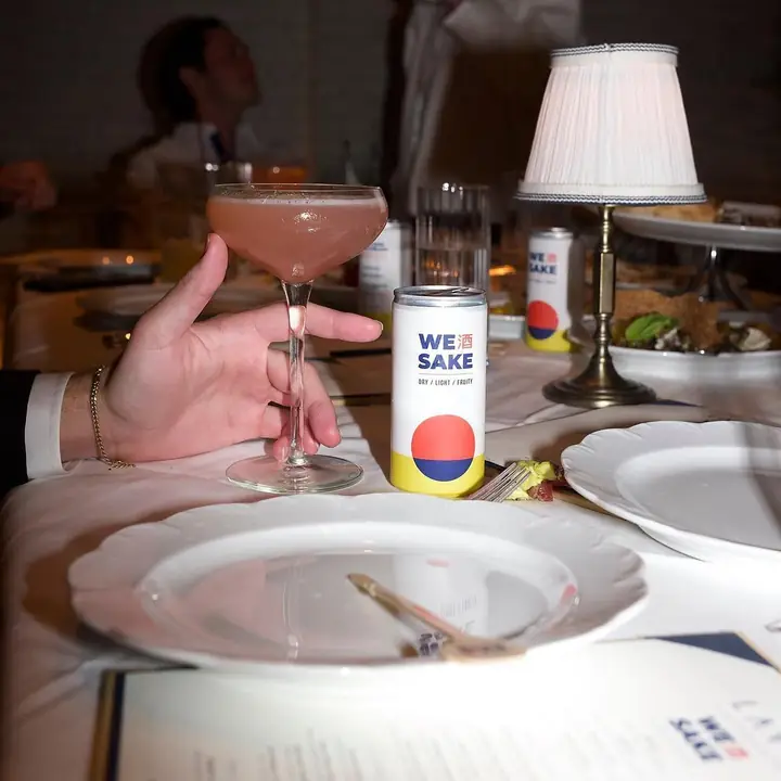 A pink sakura cocktail and a WESAKE can on a candlelit dinner table